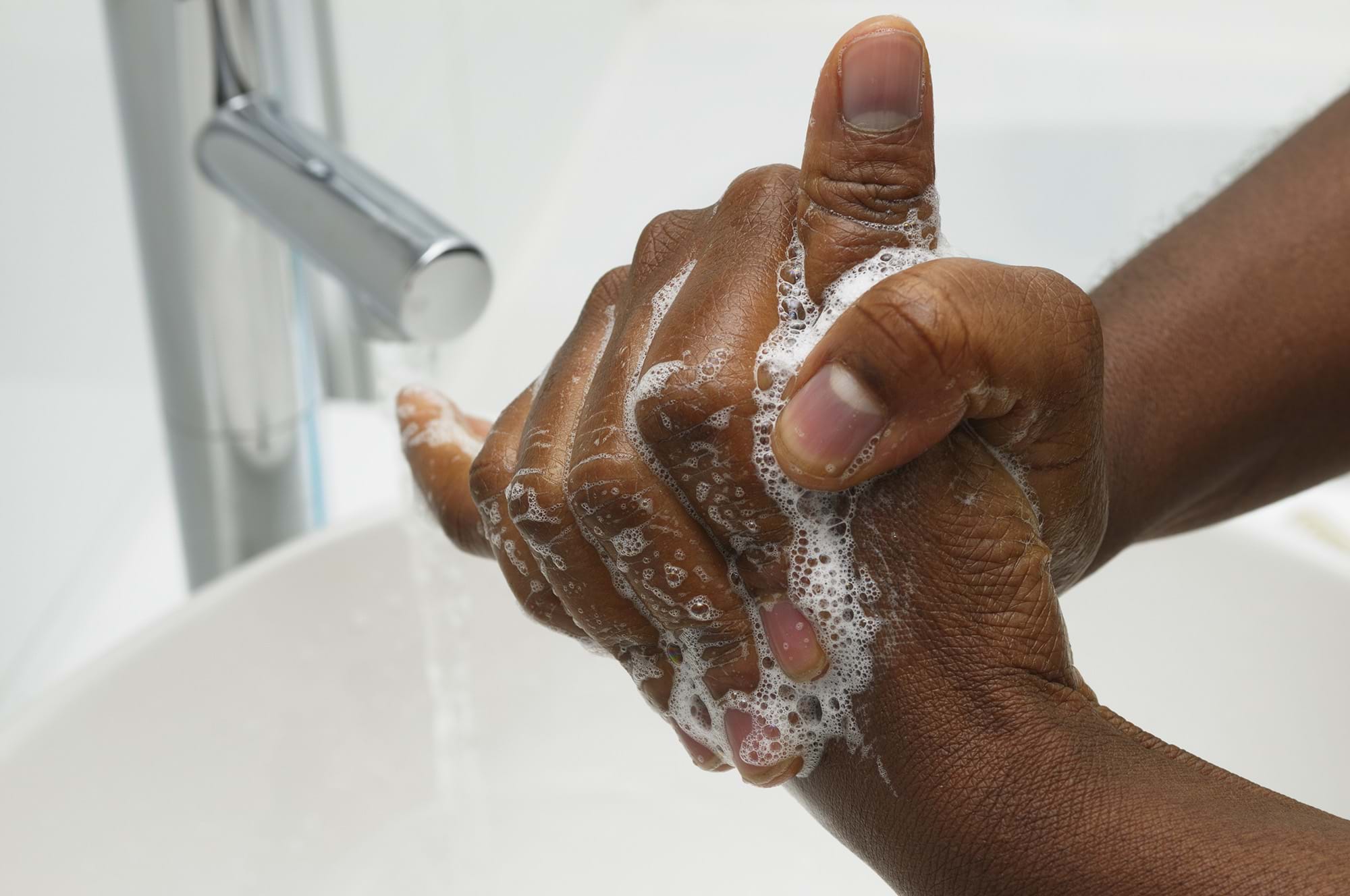 Male hands covered in soap bubbles as they are washed under a tap.